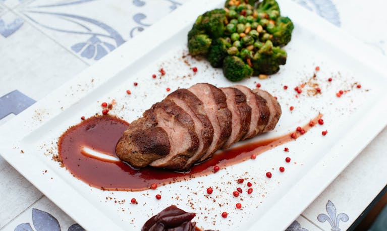 Deliciously plated duck breast with broccoli and sauce on a white plate.