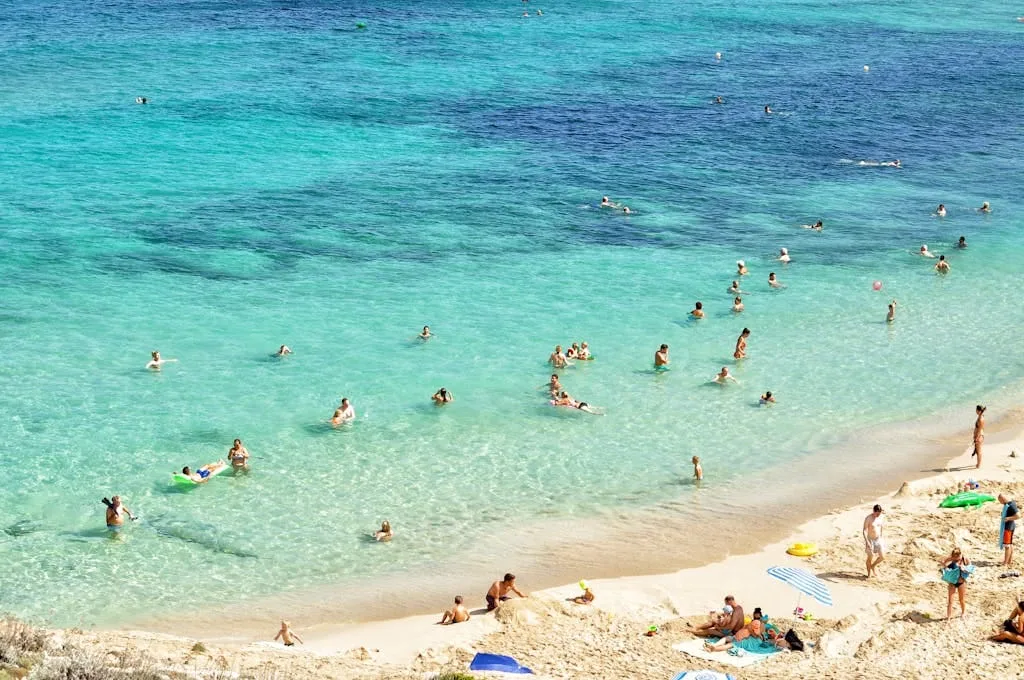 People enjoying a sunny day at a beautiful beach in Mallorca, Spain, with turquoise water and sandy shores. Majorque