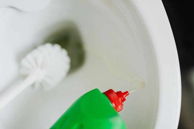 Green bottle pouring cleaner into toilet bowl with a brush beside it, emphasizing bathroom hygiene.