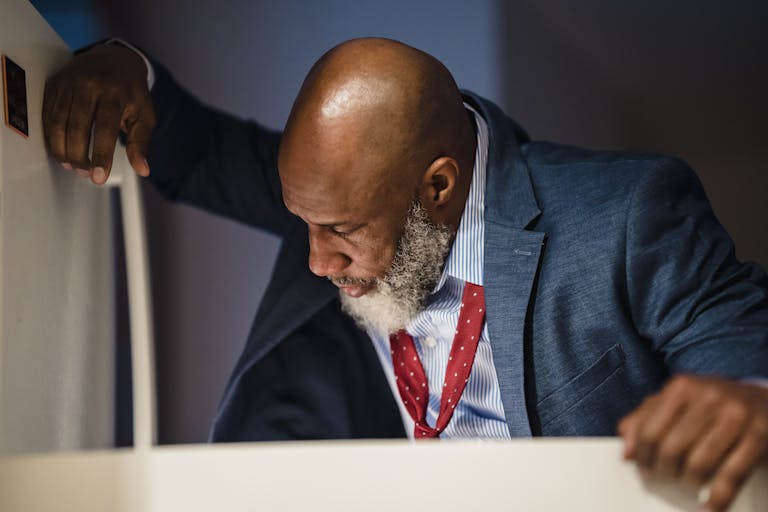 An adult man in a suit looks into an office refrigerator during the daytime.