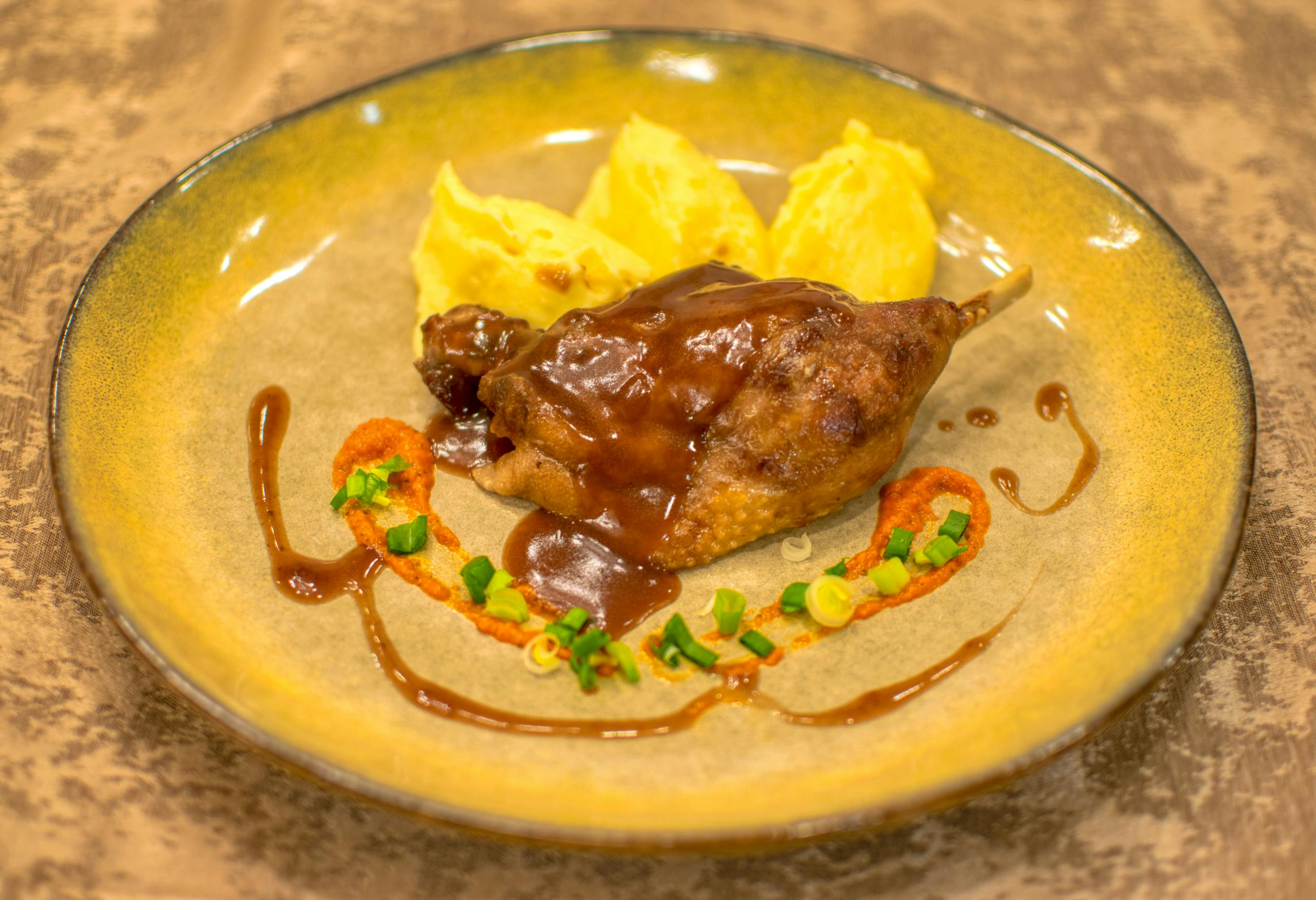 Succulent duck leg with rich sauce and creamy mashed potatoes on a rustic plate.