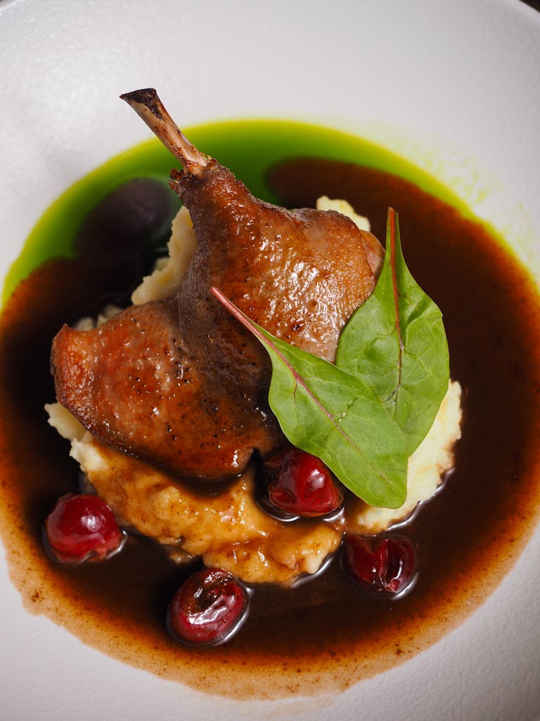 Succulent roasted duck leg on creamy mash with cherry sauce, garnished with greens.