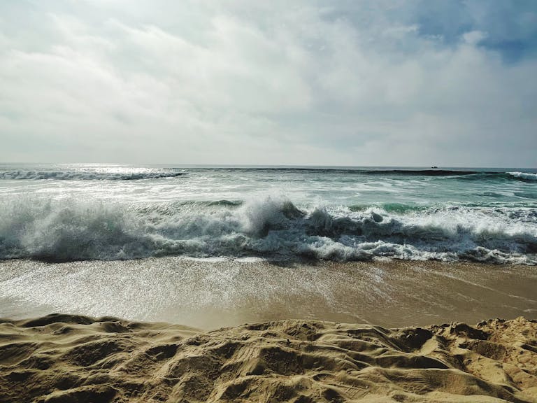 Tranquil waves crash on sandy beaches of Biscarrosse, France, under a cloudy sky.