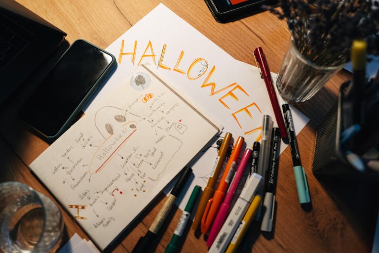 A creative workspace with Halloween-themed drawings and colorful pens on a wooden table.