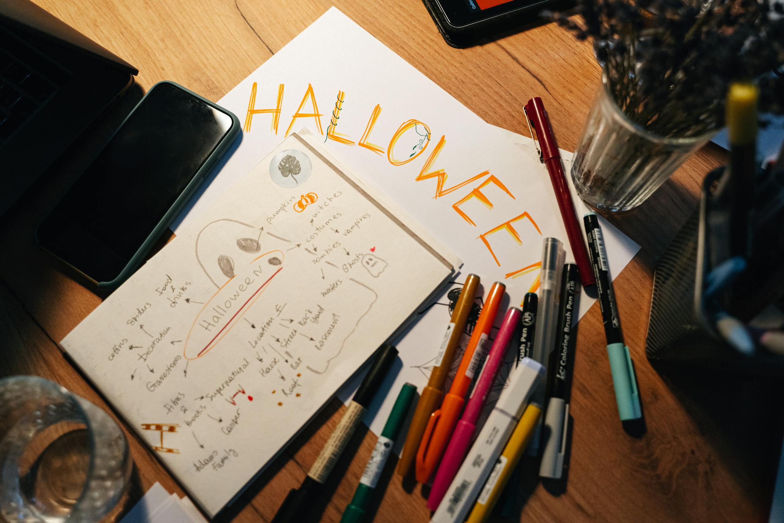 A creative workspace with Halloween-themed drawings and colorful pens on a wooden table.
