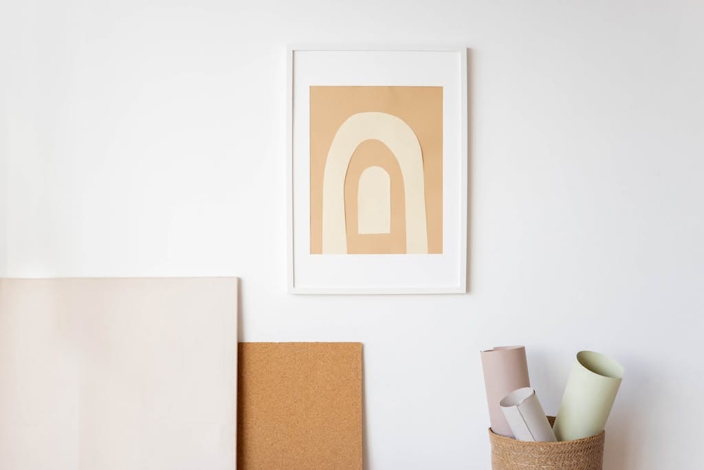 A minimalist wall setup showcasing modern abstract artwork with canvas rolls and cork board.