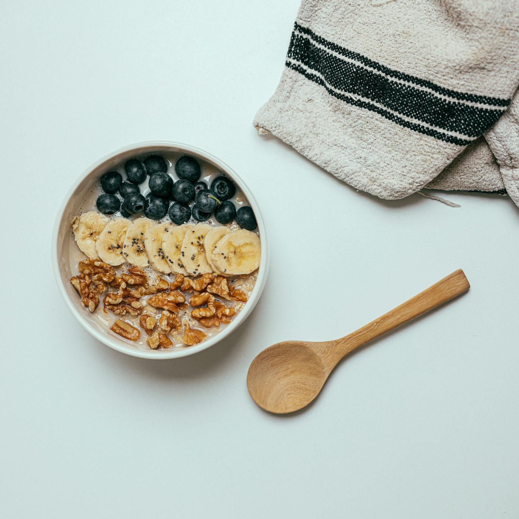A nutritious breakfast bowl featuring bananas, blueberries, and walnuts displayed in a flatlay style.