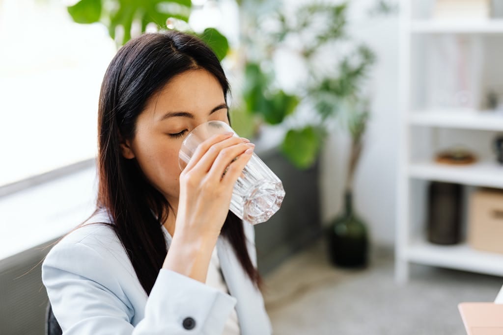 Adult woman sipping water from a glass in a modern office setting.