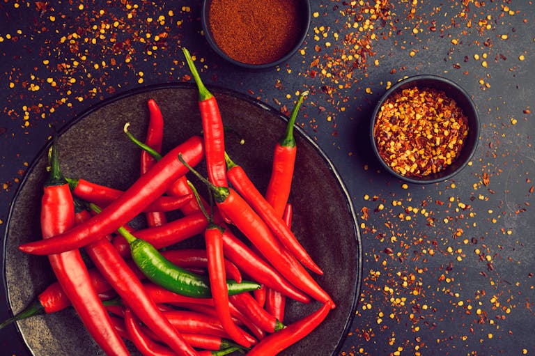 Close-up of fresh red and green chili peppers in a bowl with spices and pepper flakes.