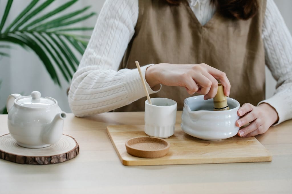 Close-up of woman preparing tea with a mortar and pestle on a wooden board indoors.